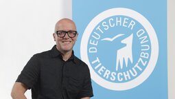 Porträt von Ralf Schneider, der vor dem Logo des Deutschen Tierschutzbundes steht.