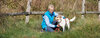 Mensch und Hund gemeinsam auf einer - von einem Holzzaun umgebenen - Wiese