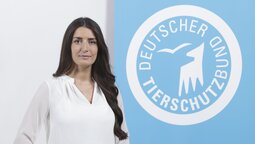 Porträt von Derya Özdemir, die vor dem Logo des Deutschen Tierschutzbundes steht