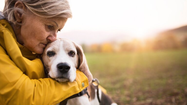 Traurig schauende ältere Frau mit Hund im Arm.