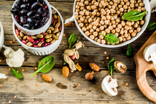 Vegane Proteinquellen auf einem Holztisch: Bohnen, Linsen, Tofu, Sojamilch,Nüsse, Samen und Gemüse