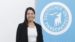 Porträt von Laura Ackermann, die vor dem Logo des Deutschen Tierschutzbundes steht.